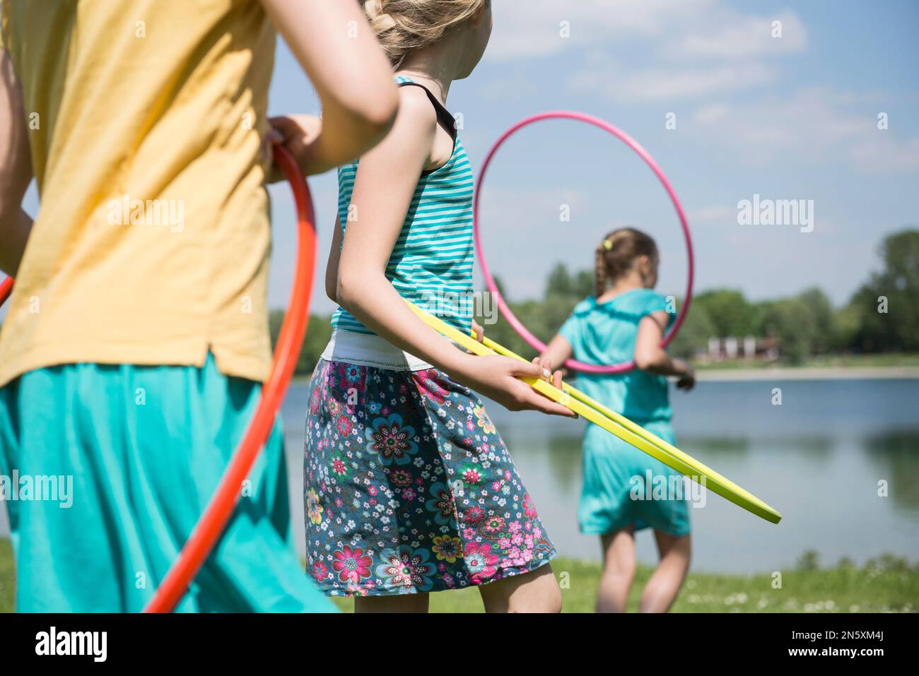 Three friends playing with plastic hoops at lakeside, Munich, Bavaria, Germany Stock Photo