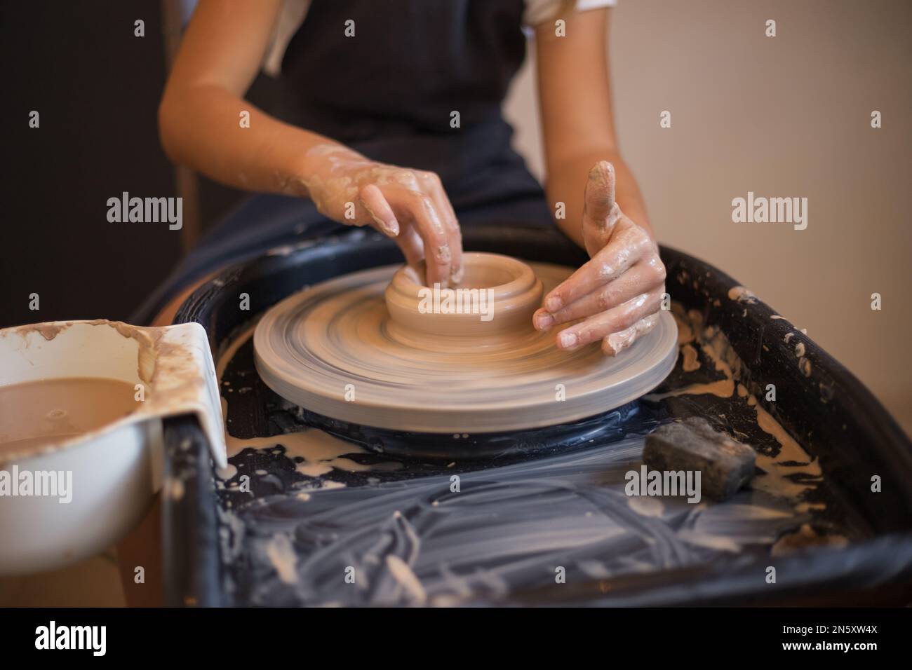 Hands of little girl creating mug on potter's wheel. Pottery wor Stock Photo