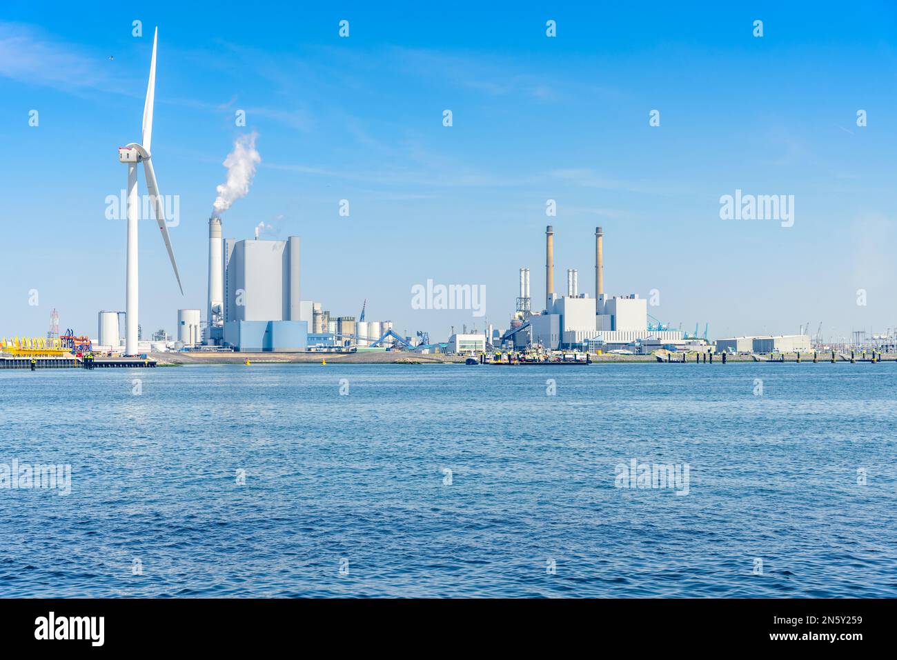 Coal fired power plants with high smokestacks on a harbour. Atall wind turbine is in foreground. Stock Photo