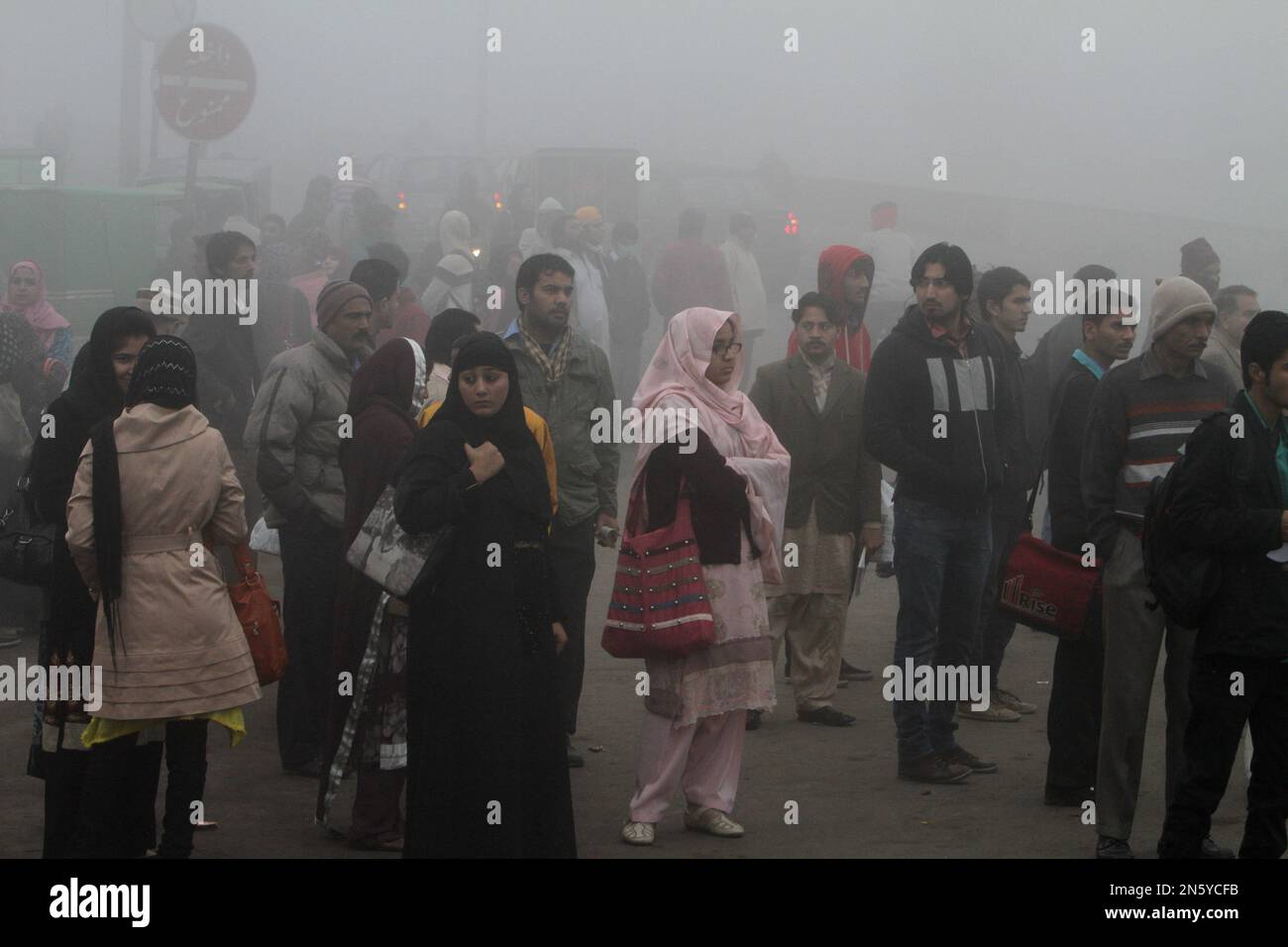 People wait for transport at a bus stop as fog envelopes Lahore