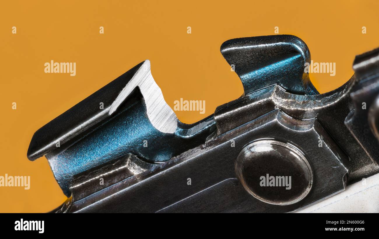 Closeup of metal saw chain link with sharp cutting edge of steel tooth on a yellow background. Modern tool detail of portable power chainsaw guide bar. Stock Photo