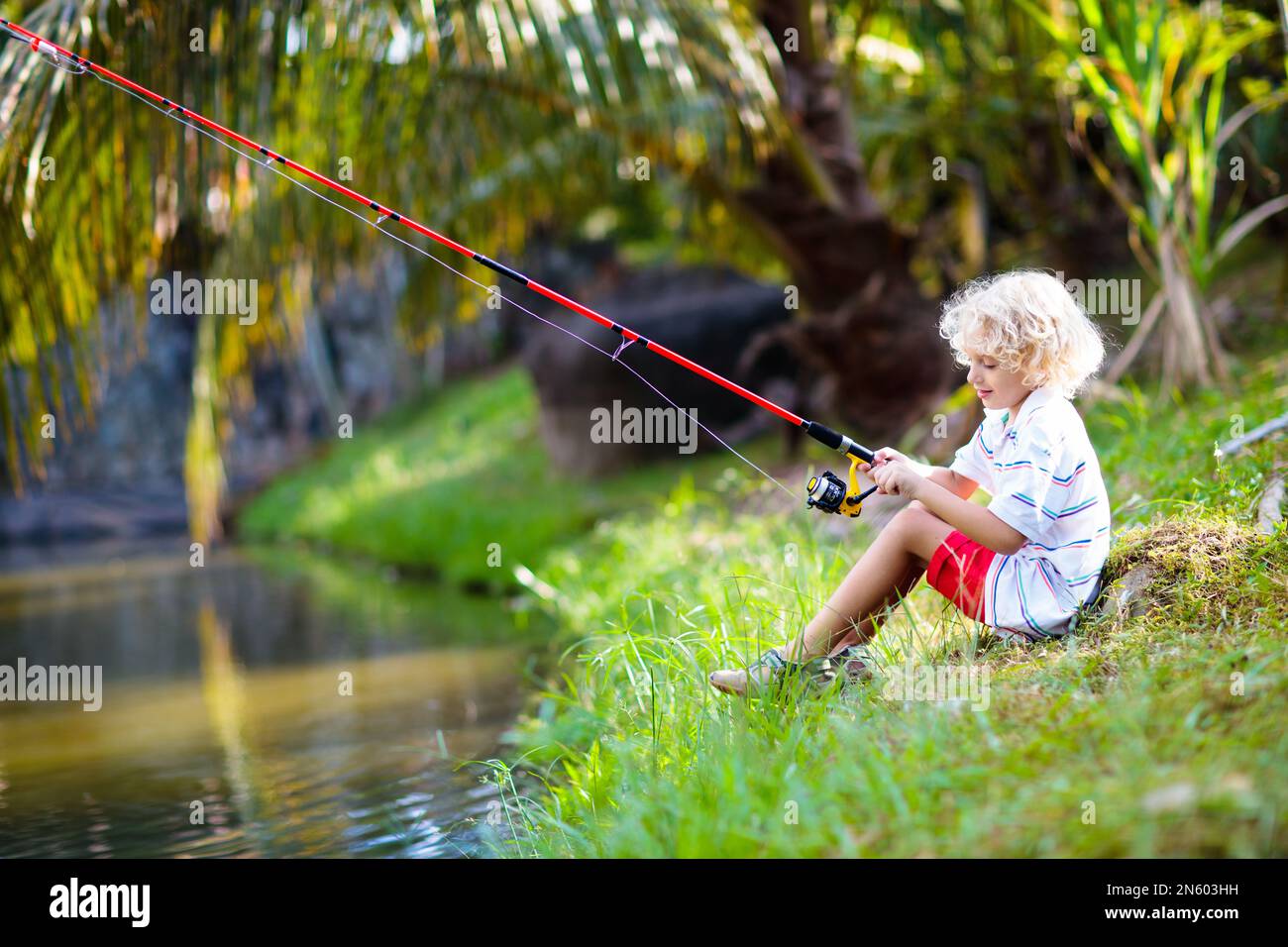 Boy fishing. Child with red rod catching fish in river on sunny summer day.  Outdoor and nature activity for kids. Little boy sitting at lake shore  Stock Photo - Alamy