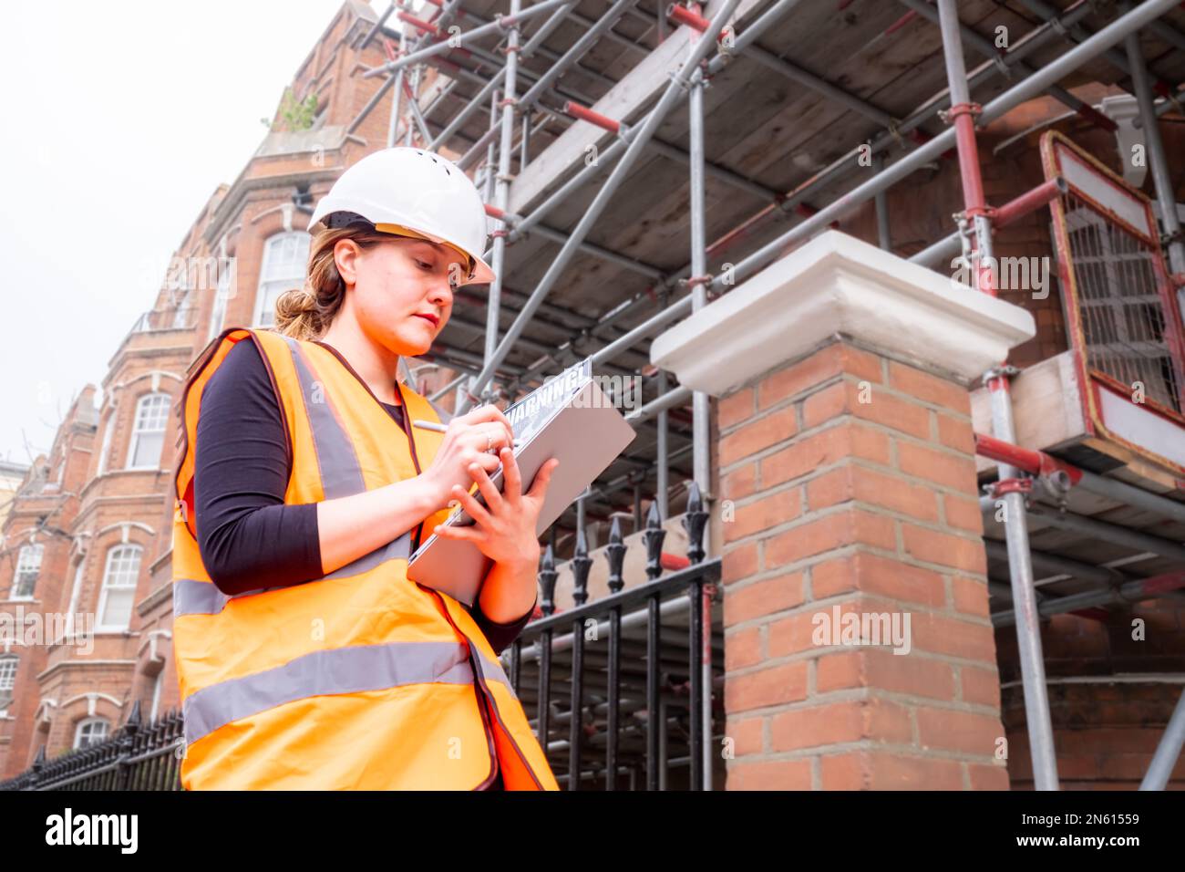 Chartered civil engineer lady writing on a tablet with electronic pen, hard hat and orange high visibility vest, inspection survey, technology Stock Photo