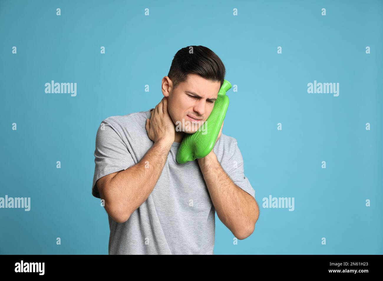 Man using hot water bottle to relieve neck pain on light blue
