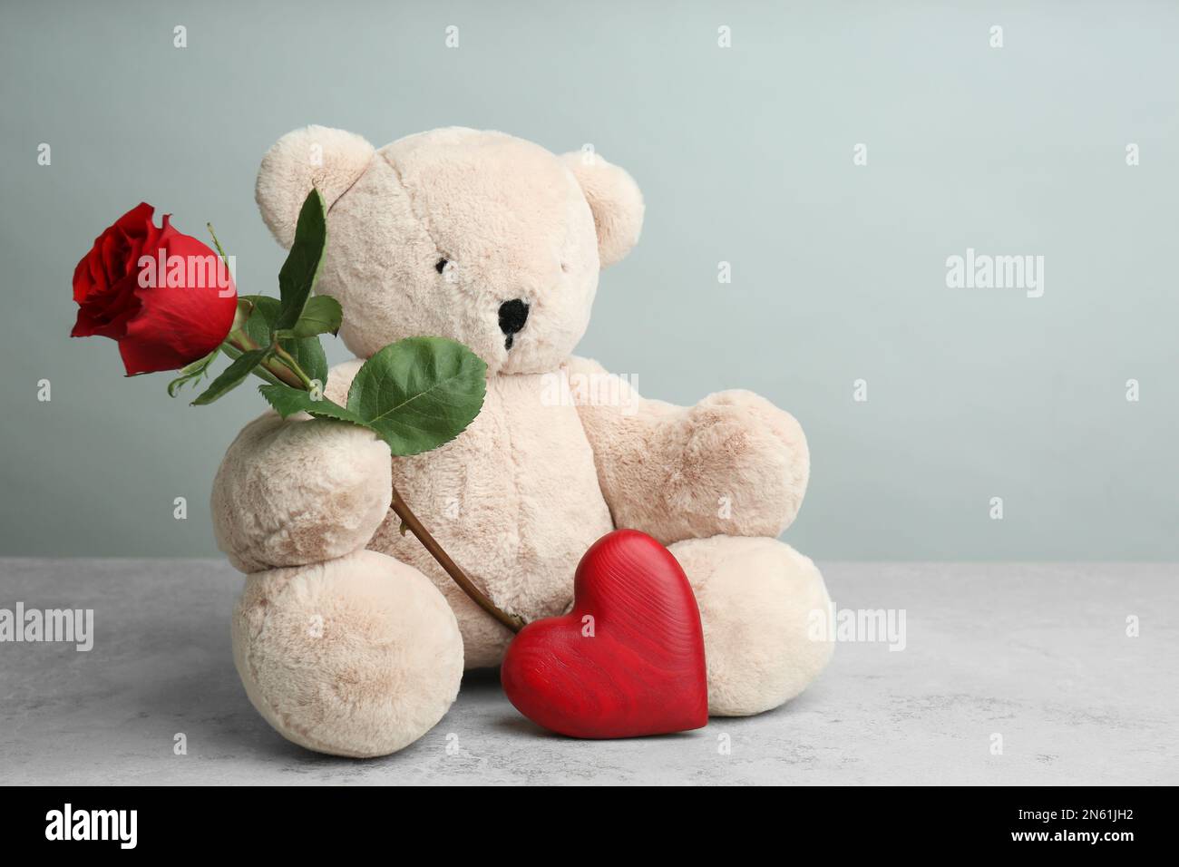 Cute teddy bear with heart and red rose on light grey stone table ...