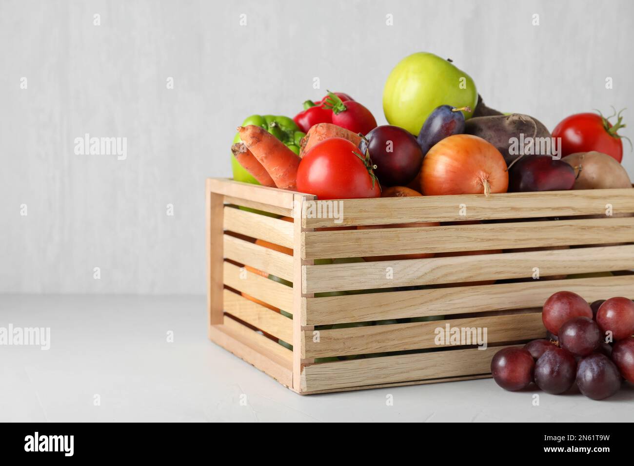 Wooden crate full of different vegetables and fruits on light table ...