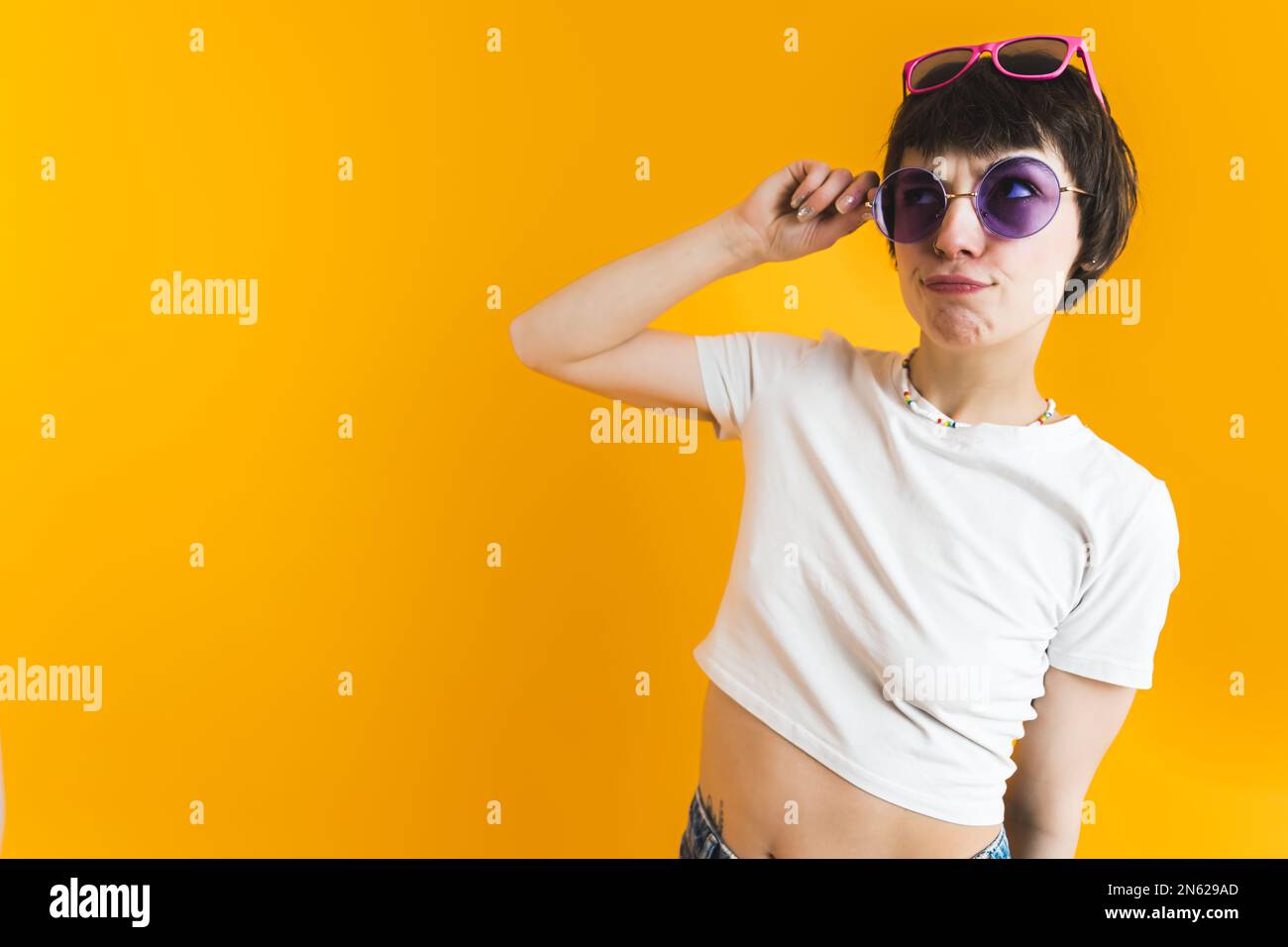 Positive young woman with multiple sunglasses on her head doing funny facial expressions and looking at copy space. Studio shot over orange background. High quality photo Stock Photo