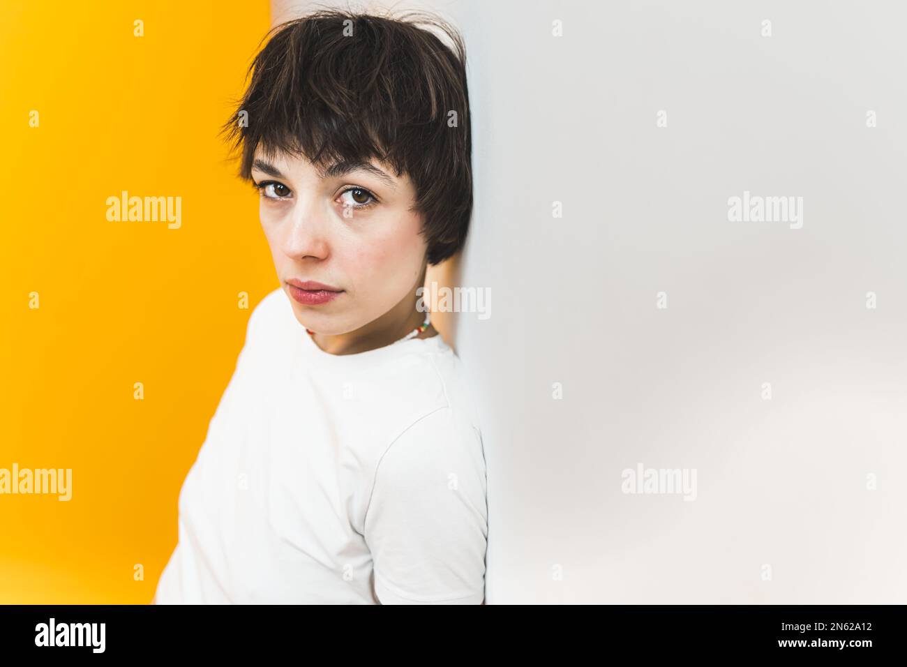 Female student looking seriously at the camera and leaning back on white wall. Studio shot. Copy space over yellow background. High quality photo Stock Photo