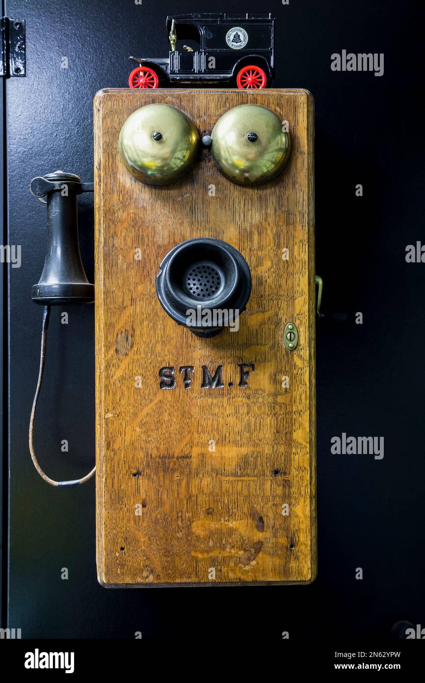 Antique circa 1910 oak wood and black bakelite plain front wall mounted telephone with brass ringing bells in garage inside old 1927 home. Stock Photo