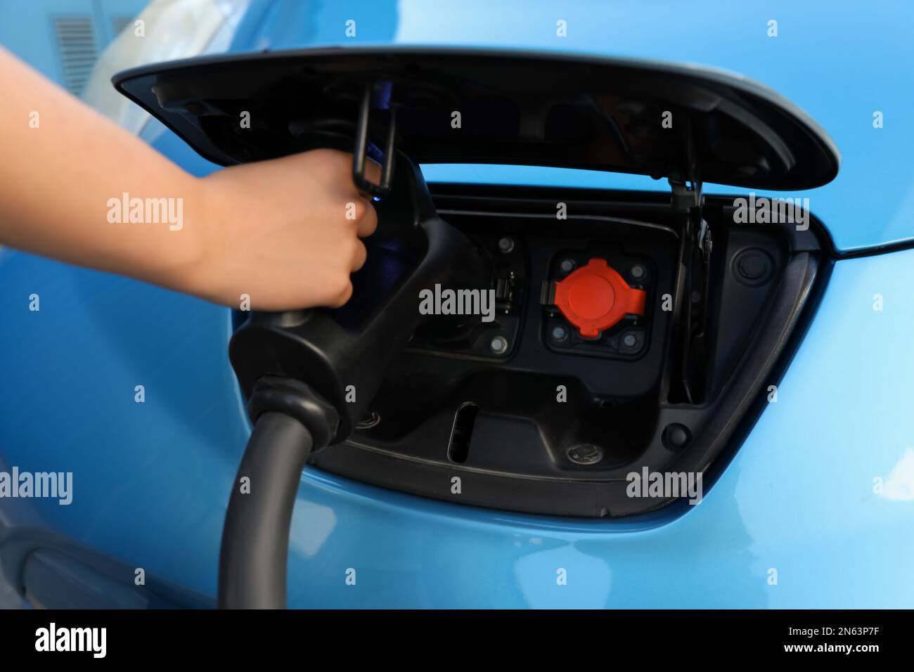 Woman inserting plug into electric car socket at charging station