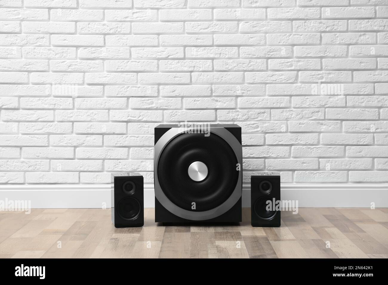 Modern powerful audio speaker system on floor near white brick wall