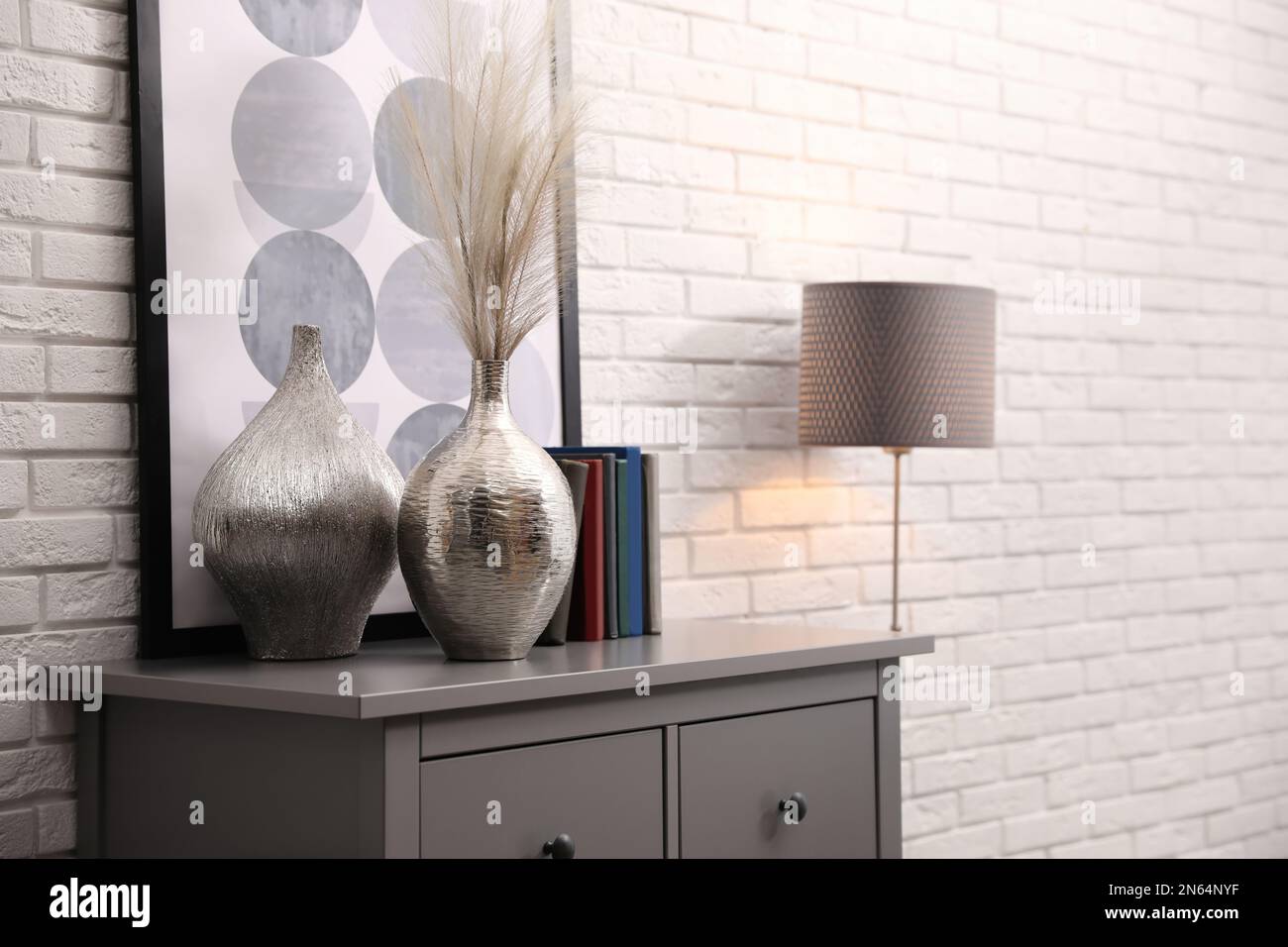 Grey chest of drawers with decor and books near white brick wall