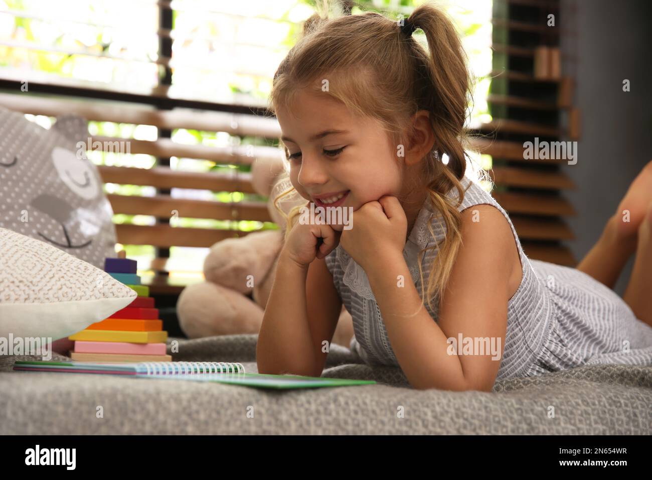 Cute little girl reading book near window at home Stock Photo - Alamy