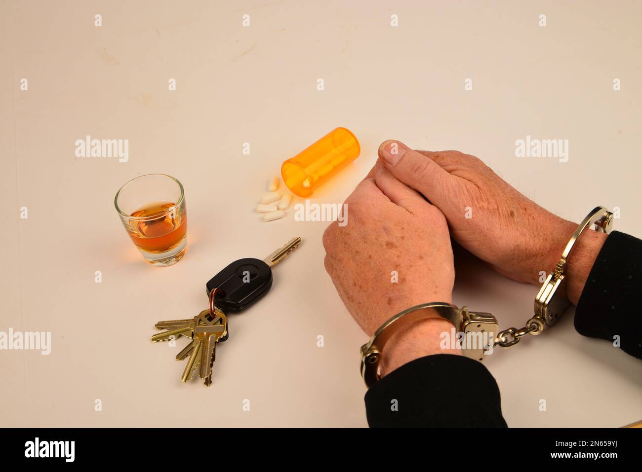 Handcuffed wrists with vehicle keys and alcohol containers symbols of substance use and driving. Stock Photo