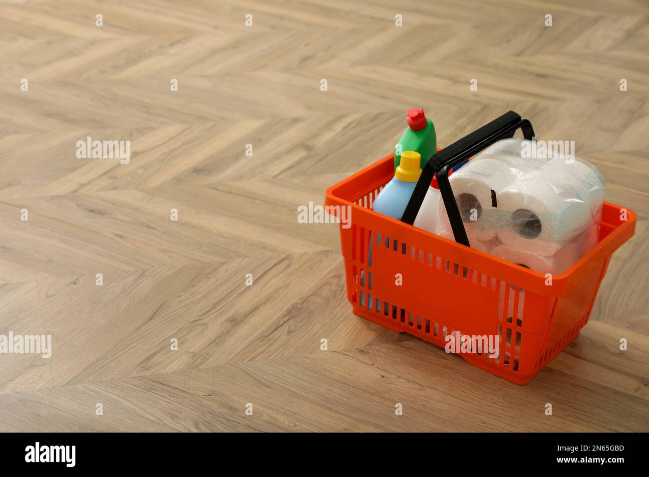 Shopping basket with household goods on wooden floor. Space for text Stock Photo