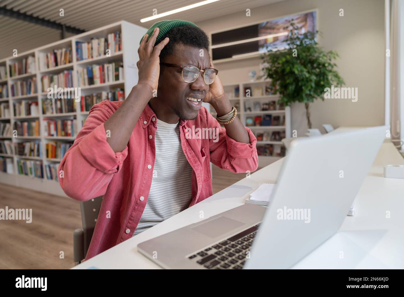Frustrated student guy in library looking at laptop having tech problems during online learning Stock Photo