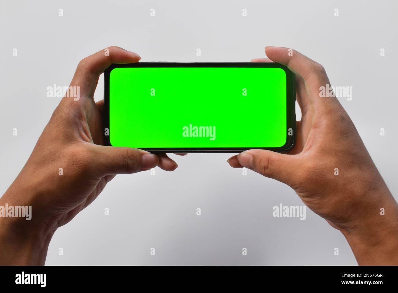 Man holds in two hands smartphone in landscape mode with green screen isolated on white background. Stock Photo