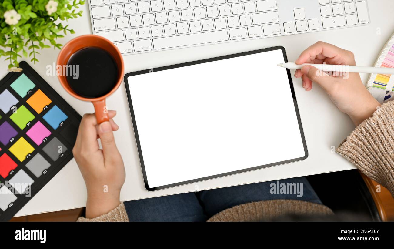 Top view of a professional female graphic designer or editor sipping coffee, designing her graphic artwork on digital tablet, working at her desk. tab Stock Photo