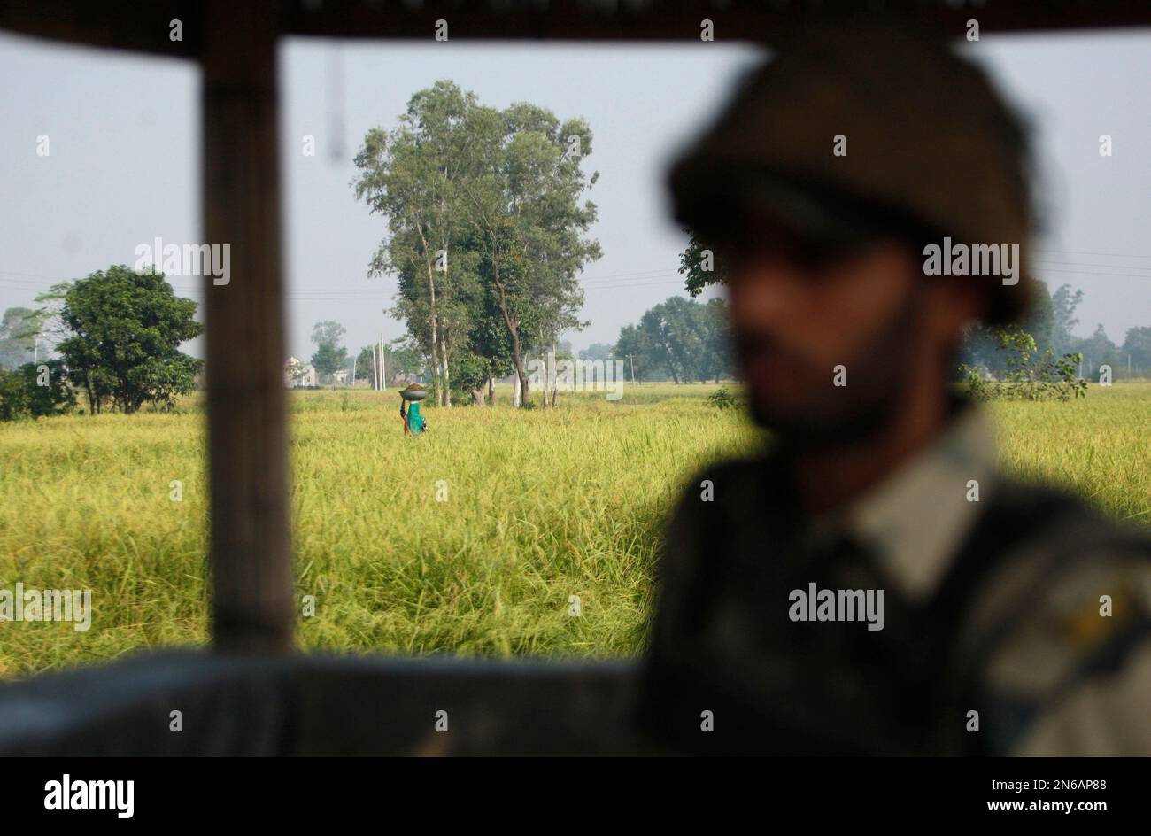 An Indian village woman walks in a field as an Indian Border Security Force  soldier stands guard at the India-Pakistan international border area at  Aria, about 42 kilometers (26 miles) south of