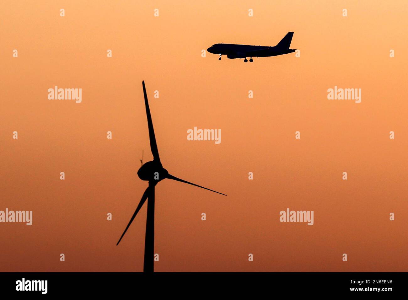 Airplane silhouetted flying past a wind turbine at early dawning. Stock Photo