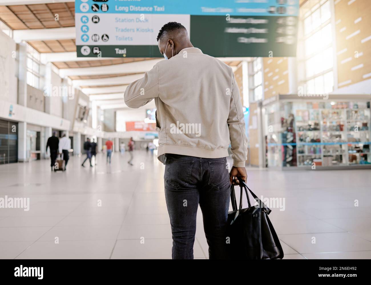 Rear view of African american businessman travelling alone and standing in a train station while checking his travel times on his watch Stock Photo