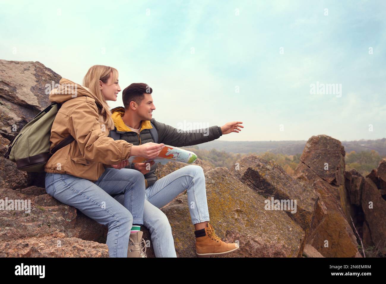 Couple of travelers with backpacks and map sitting on steep cliff ...