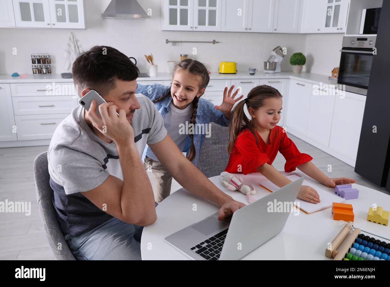 Children disturbing stressed man in kitchen. Working from home during ...