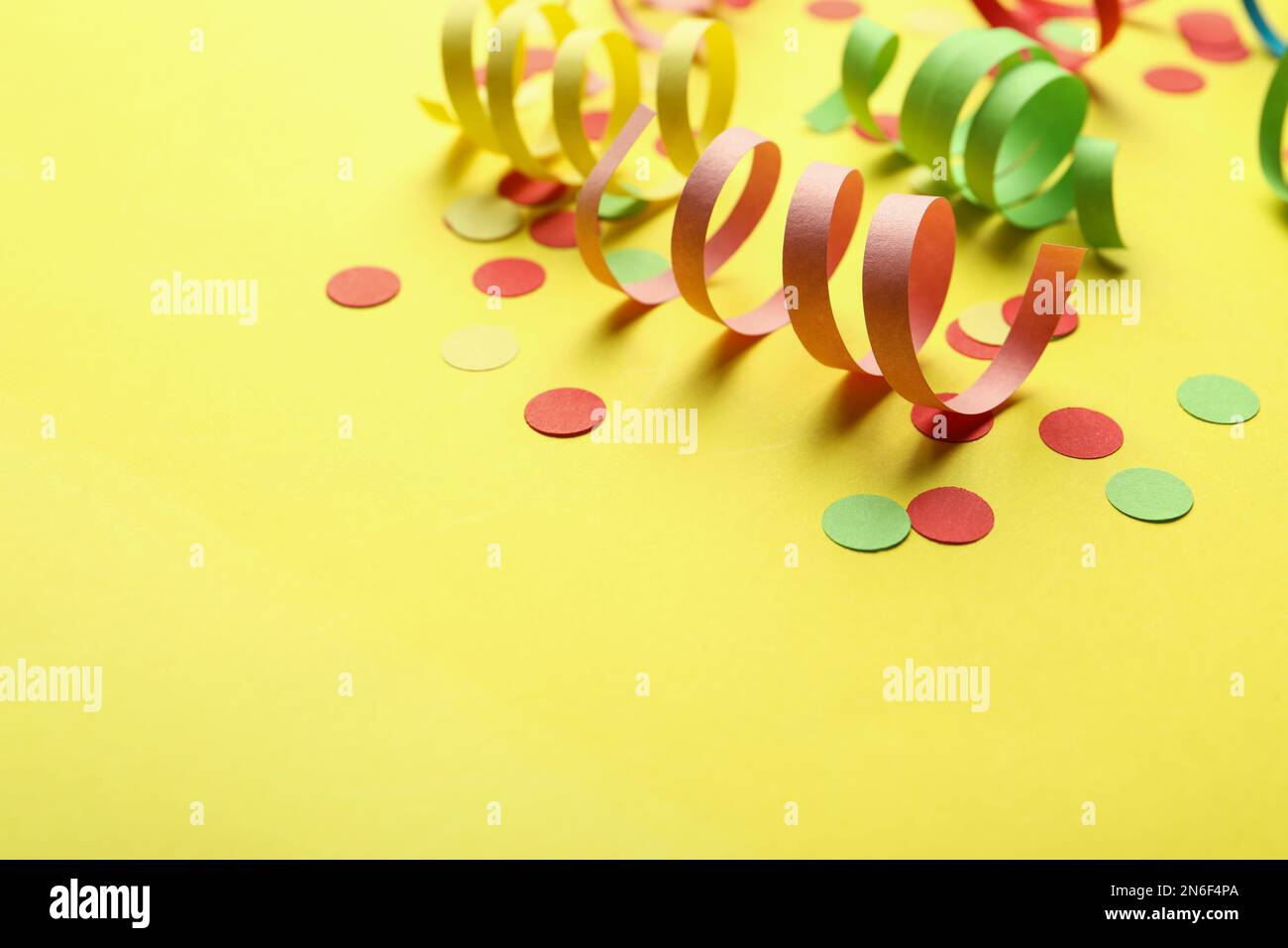 Colorful serpentine streamers and confetti on yellow background. Space