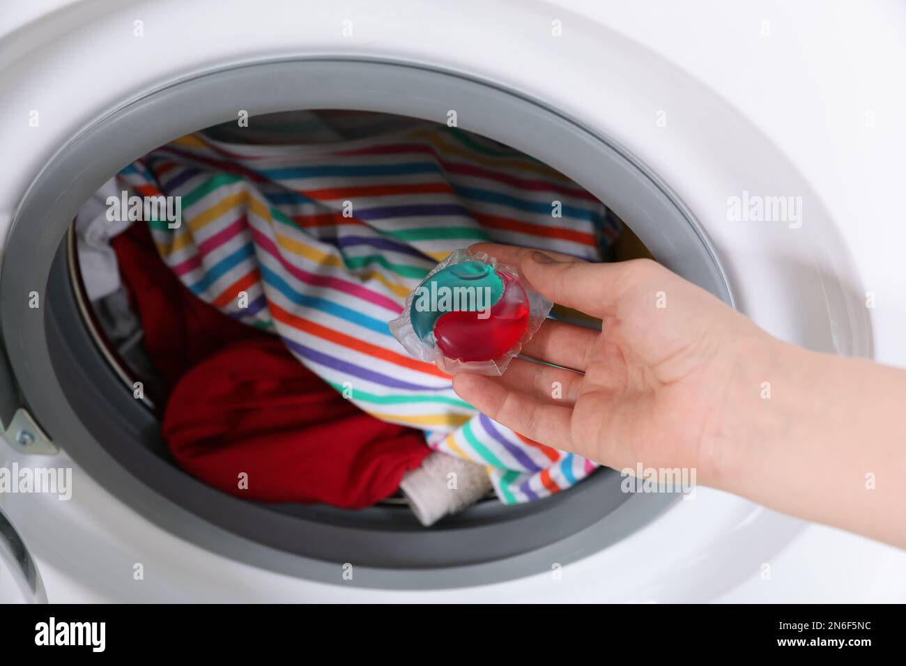 Woman putting laundry detergent capsule into washing machine, closeup