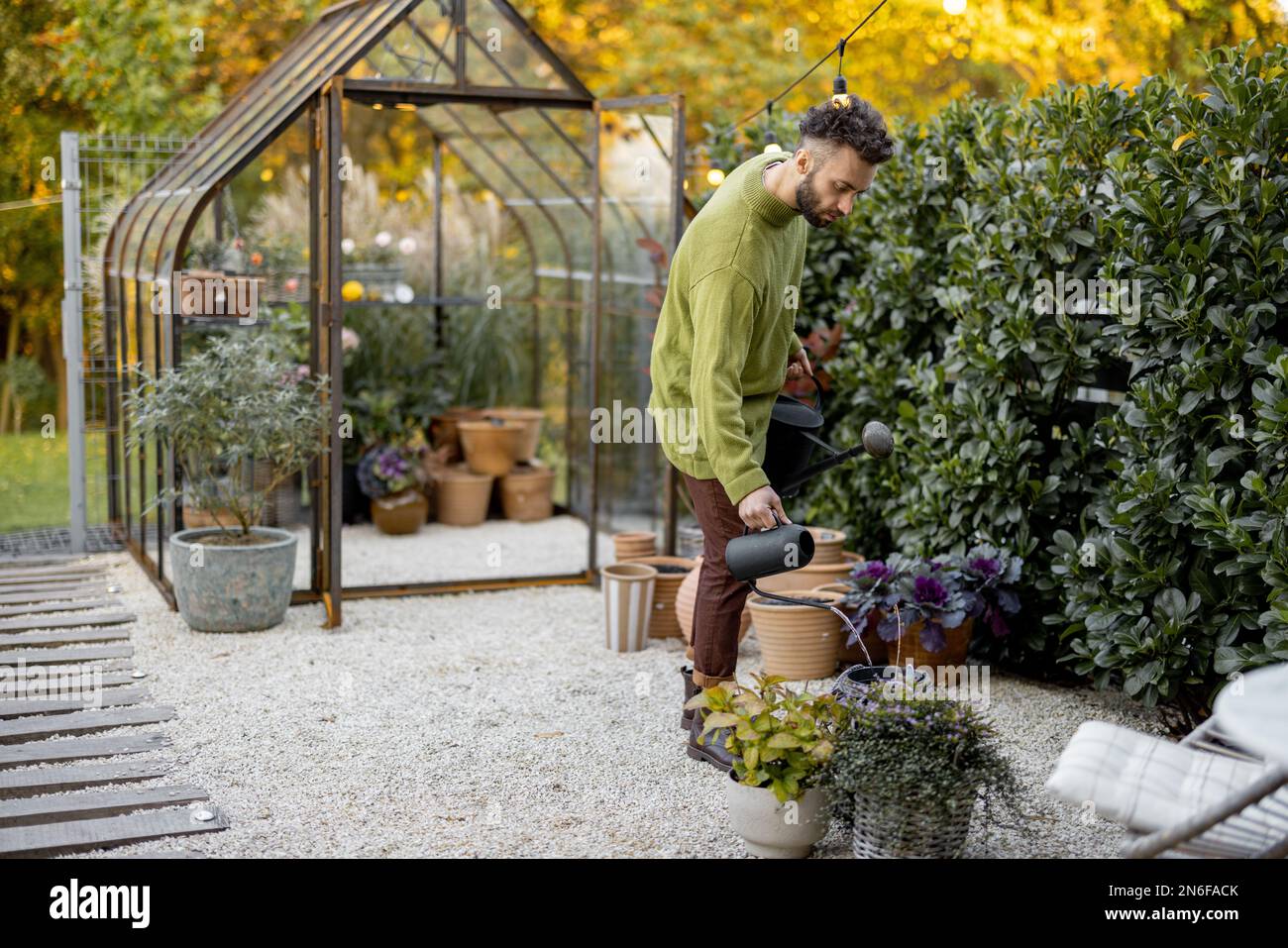 Stylish guy with watering can in garden Stock Photo