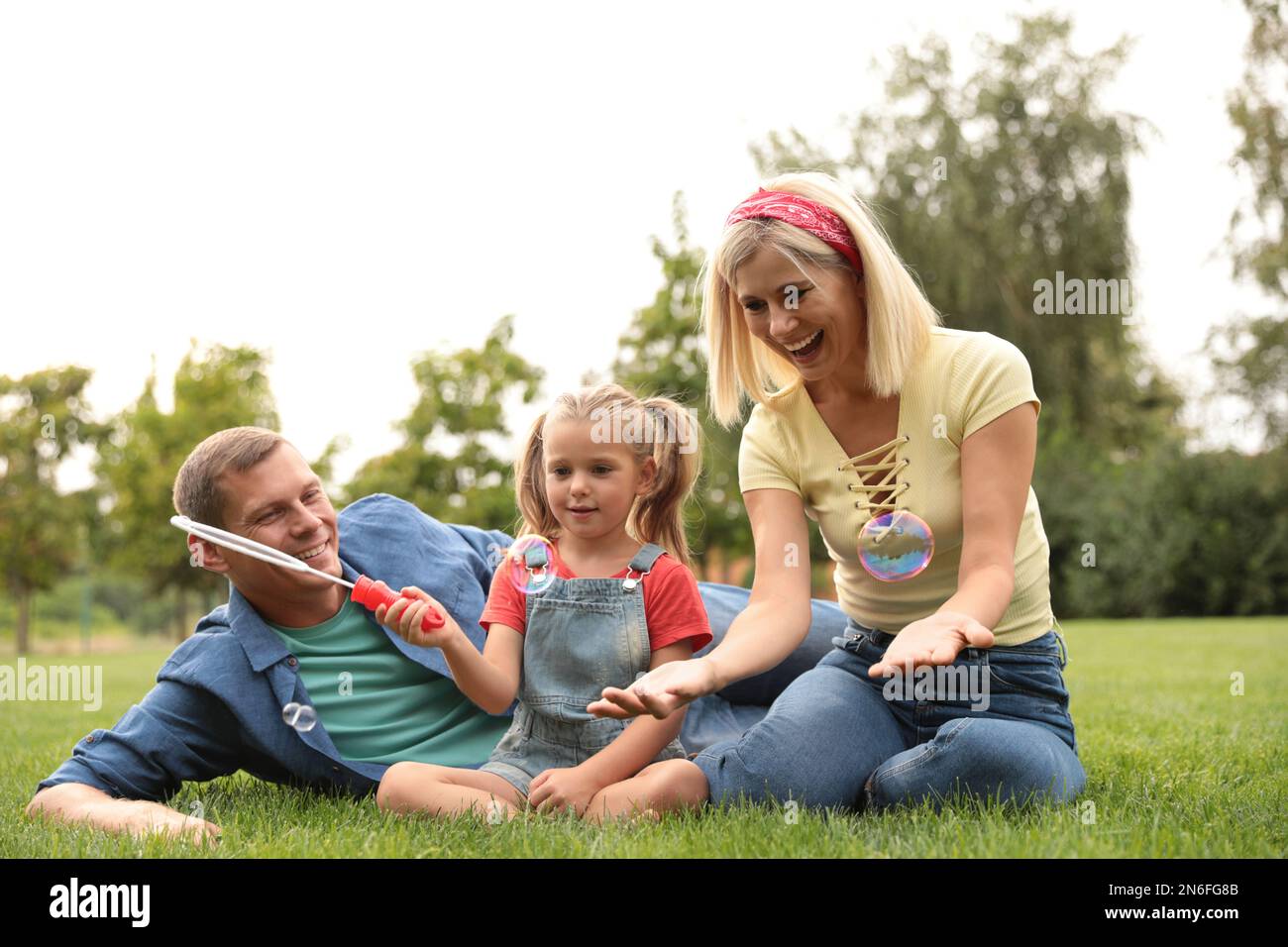 Happy family blowing soap bubbles in park on green grass Stock Photo ...