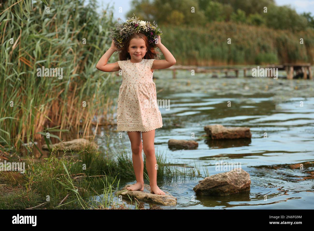 Cute little girl wearing wreath made of beautiful flowers near river ...