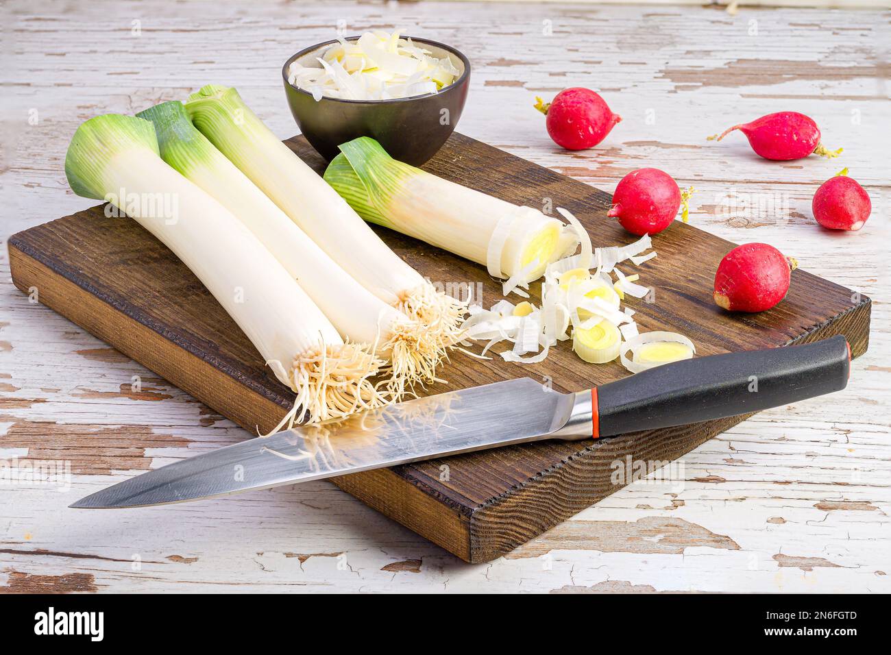 Some leeks on a wooden board with a knife and radishes around Stock Photo