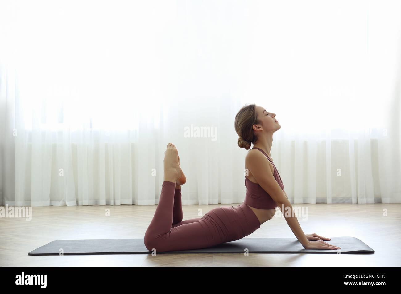 Young woman practicing king cobra asana in yoga studio. Raja