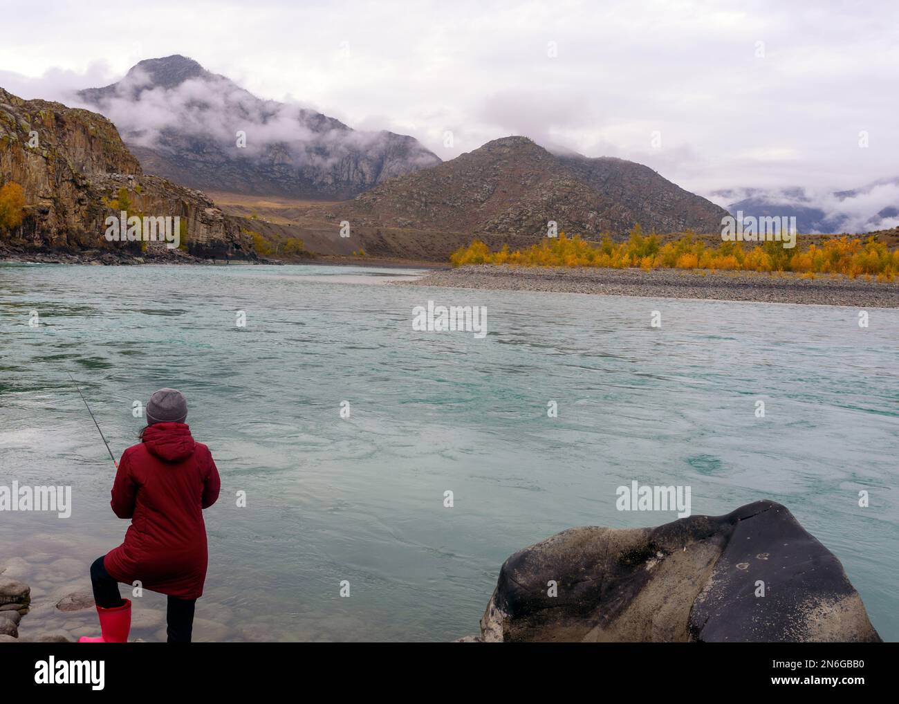 A girl fisherman stands on the bank of the mountain river Katun with a fishing rod in the Altai in the morning. Stock Photo