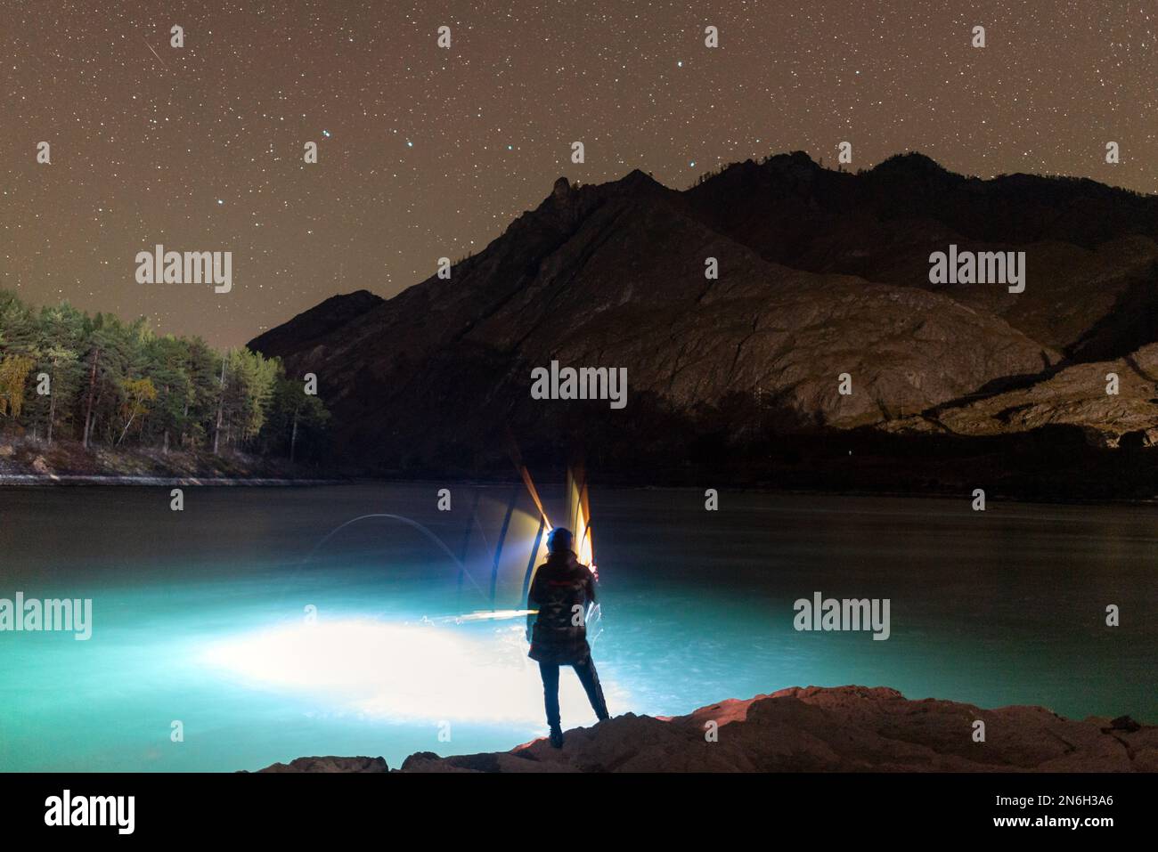 The silhouette of a fisherman girl with a lantern waves a fishing rod at  night on the river bank under a rock with stars in Altai Stock Photo - Alamy