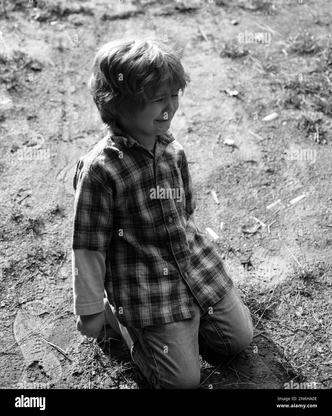 A toddler is falling down on the road. Kids emotional concept. Blonde little boy cries with tears. Upset child. Violence in family over children Stock Photo