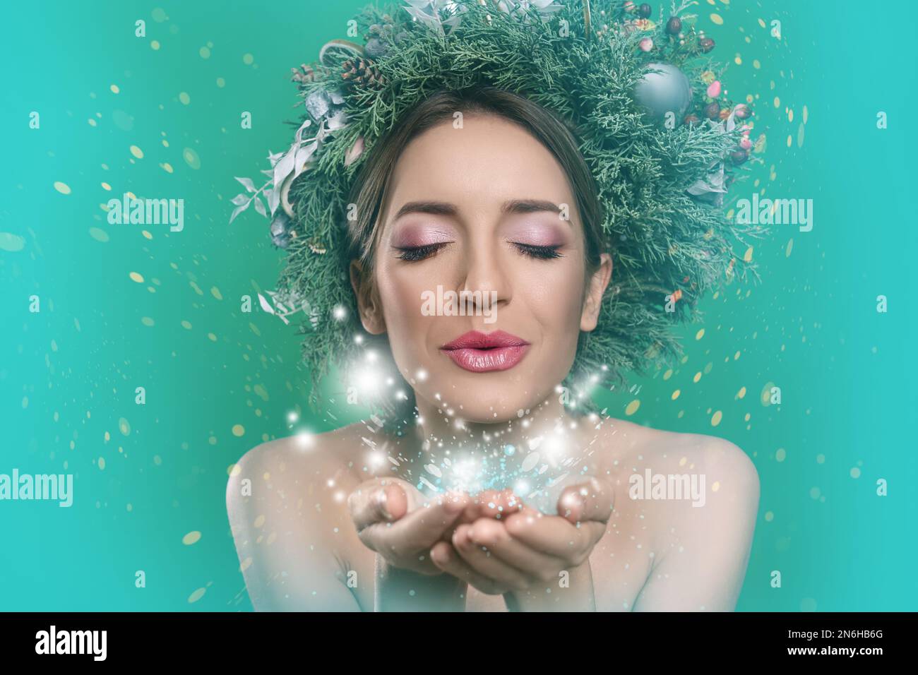 Beautiful young woman with Christmas wreath blowing kiss on color background Stock Photo
