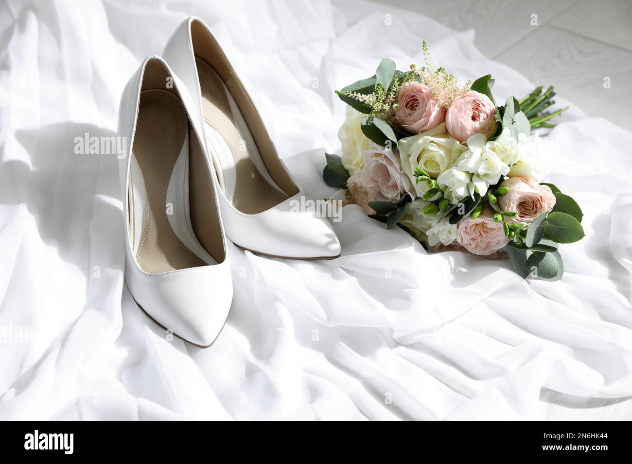 Pair of wedding high heel shoes and beautiful bouquet on white fabric Stock Photo