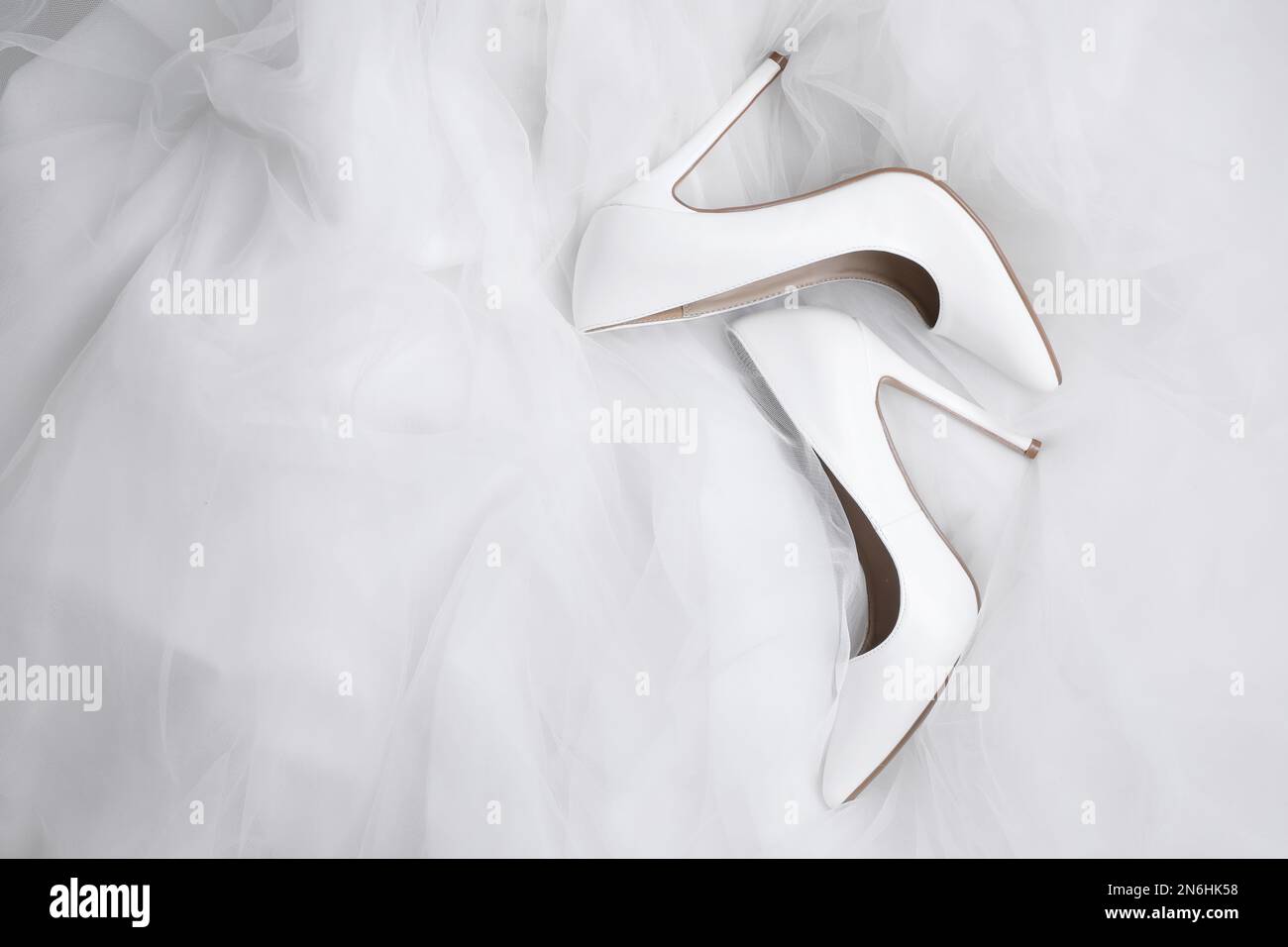 Pair of wedding high heel shoes on white veil, flat lay Stock Photo
