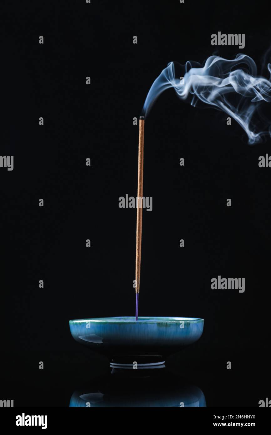 Incense stick smoldering in holder on black background Stock Photo - Alamy