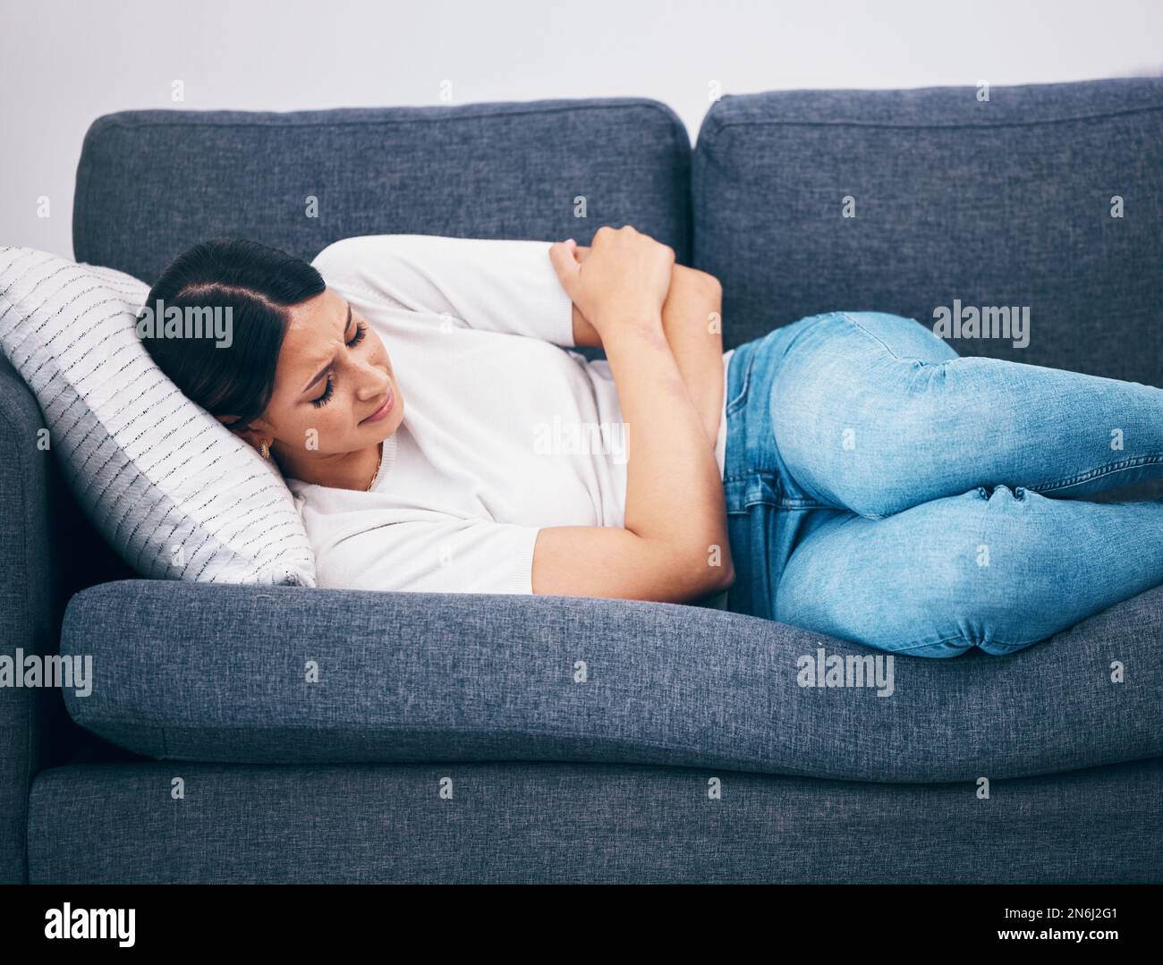 Sick, menstruation and woman with cramps on the sofa, digestion problem and pain after eating