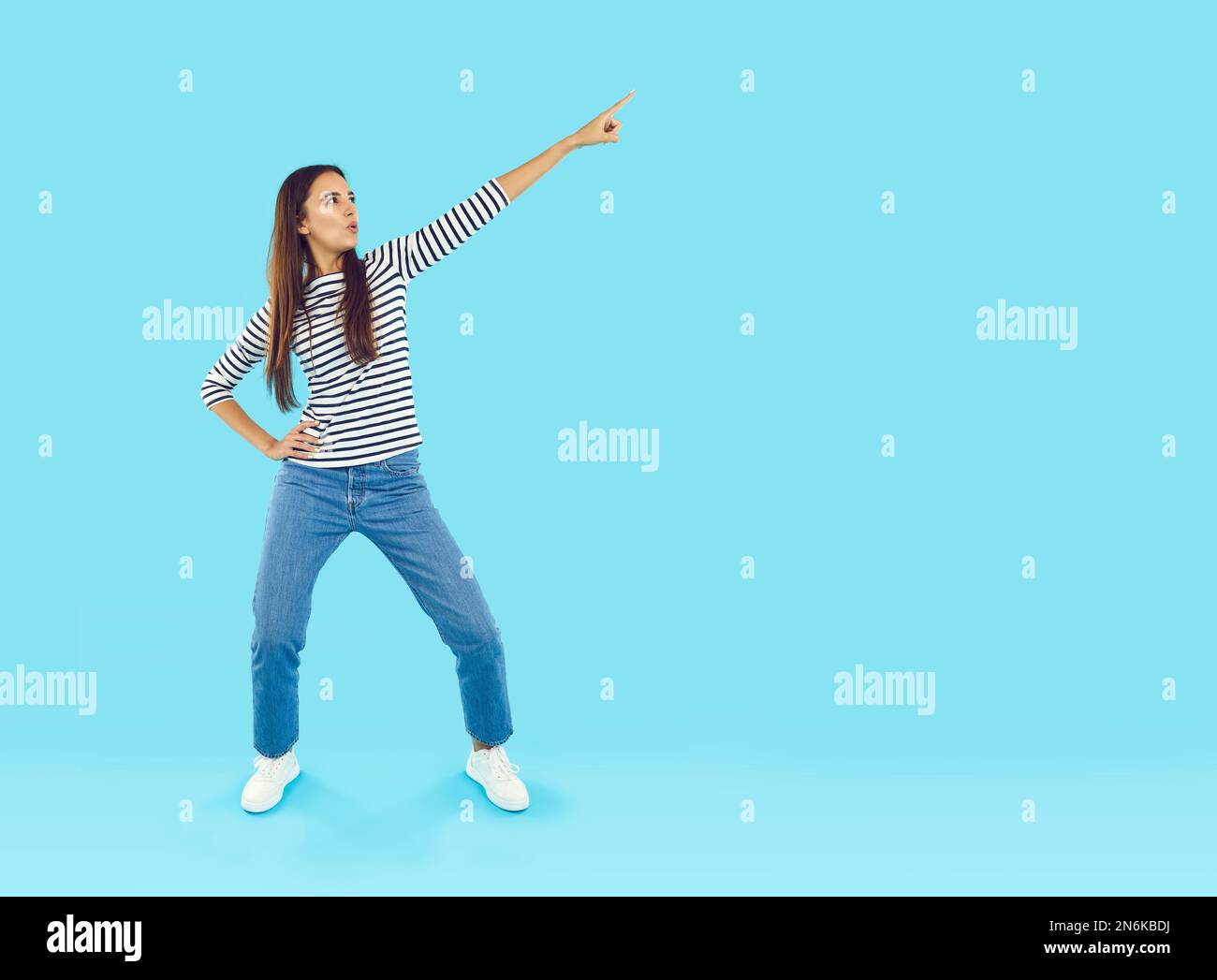 Funny woman standing on blue studio background and pointing to blank copy space side Stock Photo