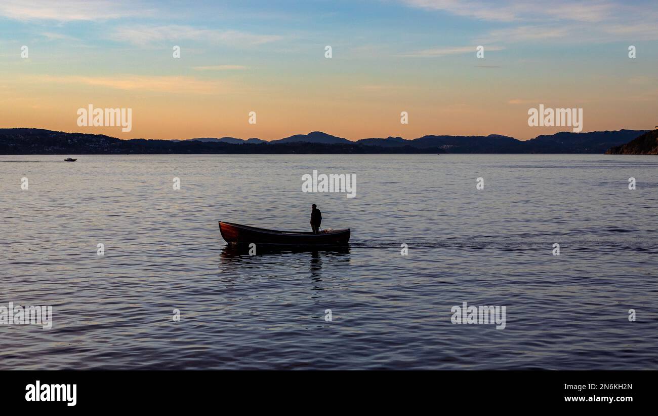 A man in a small boat, at Byfjorden, at sunset. Outside port of Bergen, Norway. Stock Photo