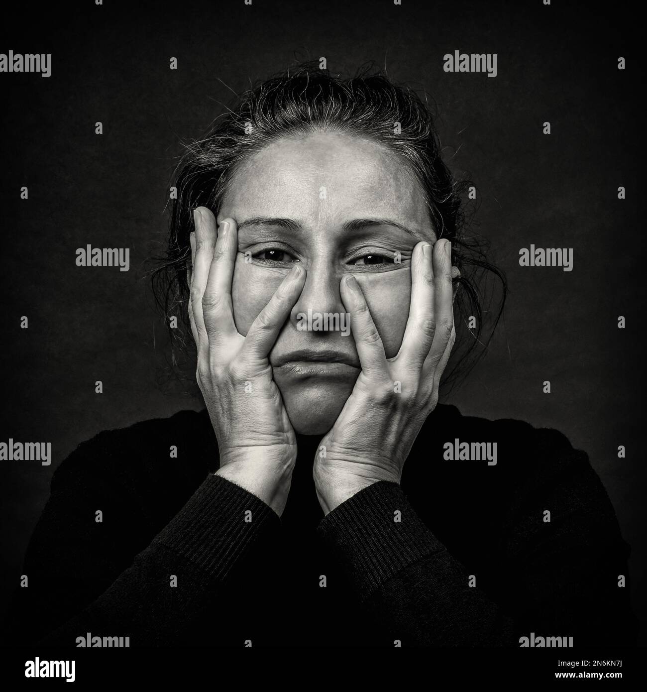 Conceptual dark portrait of old depressed woman stretching the skin of her face in ugly grimace.  Problems with skin and wrinkles, mental problems. Bl Stock Photo