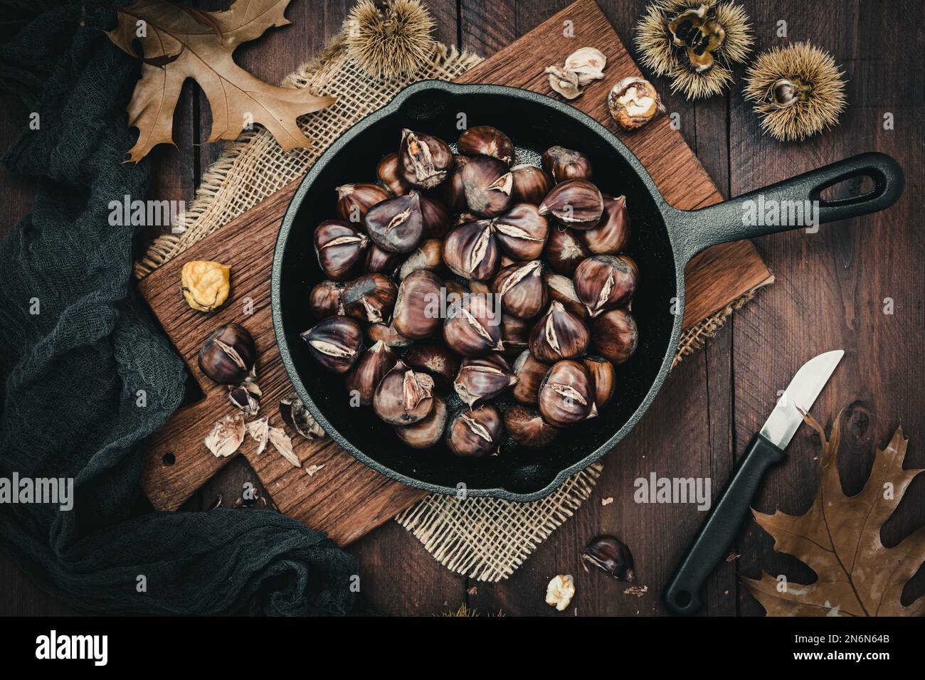 Roasted chestnuts in a cast iron pan on a wooden board, top view Stock Photo