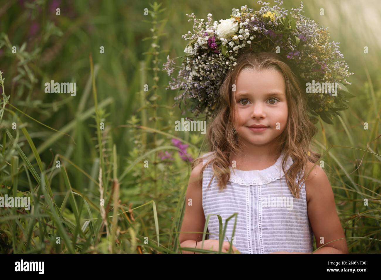 Cute little girl wearing wreath made of beautiful flowers in field ...
