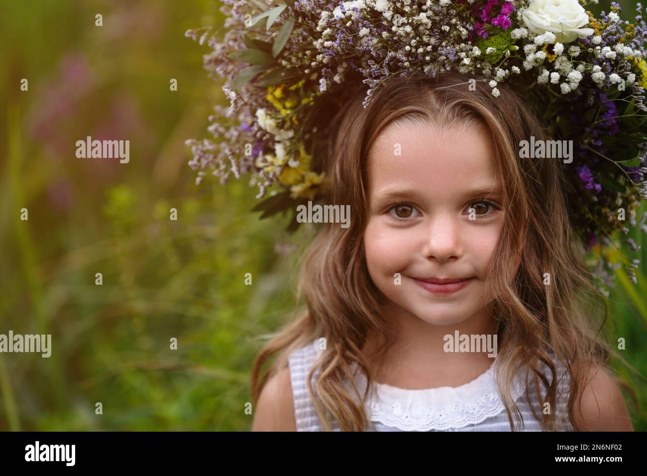 Cute little girl wearing wreath made of beautiful flowers in field ...