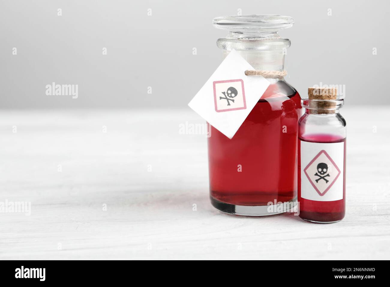 Glass bottle and vial of poison with warning signs on white wooden