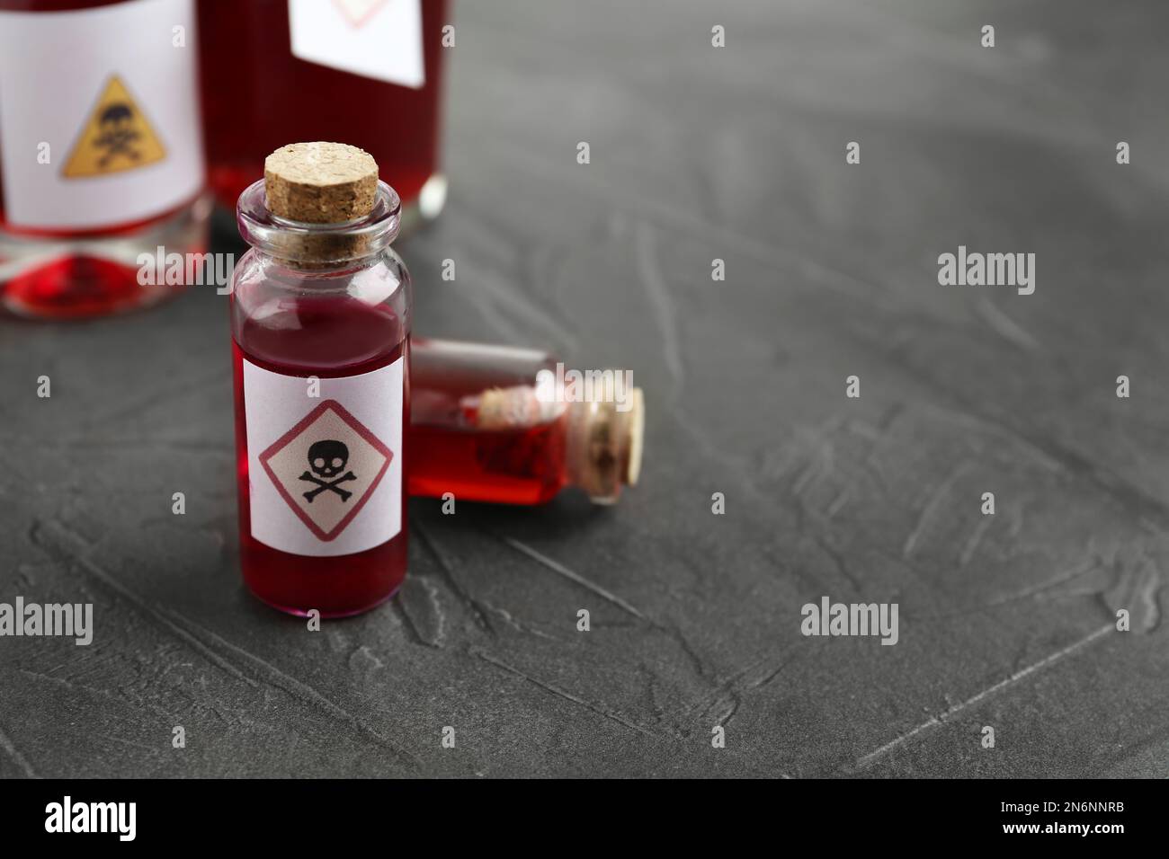 Glass vials of poison with warning sign on grey stone table, closeup
